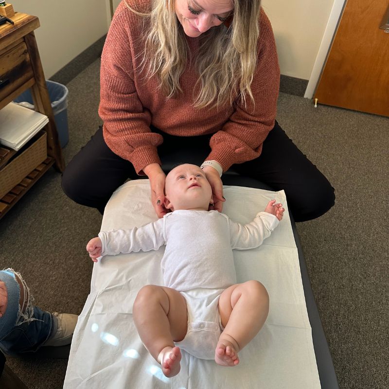 Female Infant chiropractor in Smithtown NY is performing a chiropractic adjustment on a baby in her office 